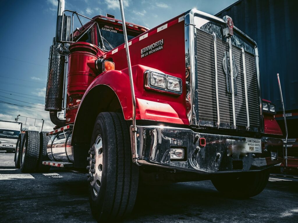 A worker in uniform inspects the large tire of a parked commercial truck in an outdoor lot.