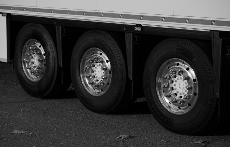 Mechanic inspecting tread depth on a large commercial truck tire with a tire gauge in a well-lit service area.