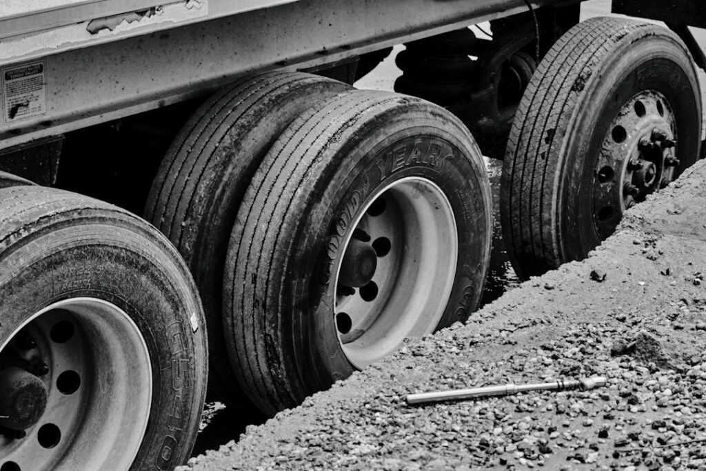 Commercial truck tire being measured with a tread depth gauge beside a wet roadway.