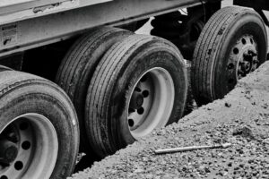 Commercial truck tire being measured with a tread depth gauge beside a wet roadway.