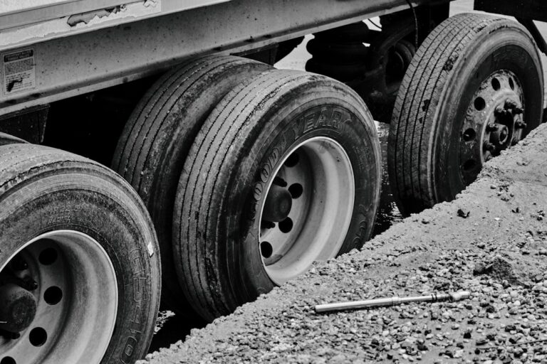 Commercial truck tire being measured with a tread depth gauge beside a wet roadway.